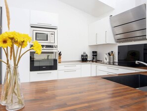A modern kitchen with white cabinets, a black countertop, a Siemens oven, a coffee maker, and a vase with yellow flowers. - 5 Star Holiday Home in Grenaa (Grenaa)