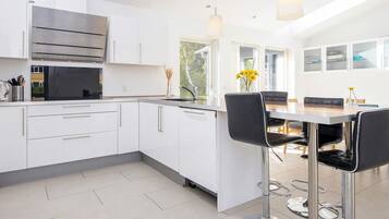 Una cocina moderna con gabinetes blancos, electrodomésticos de acero inoxidable y una zona de comedor con mesa y sillas.