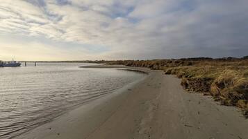 A sandy beach with a boat docked on the left, a curved shoreline, and a grassy dune area.