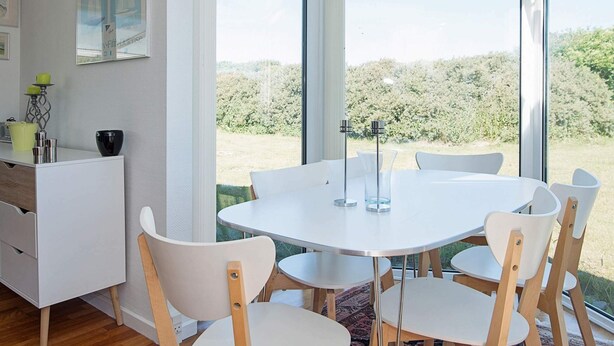 A modern dining area with a glass-enclosed table and chairs, a white cabinet, and a poster on the wall. - 4 Person Holiday Home in Lokken (Lokken)