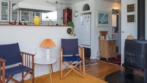 A cozy living room with a fireplace, wooden furniture, and a kitchen area with a refrigerator and a clock. - 4 Person Holiday Home in Lokken (Lokken)
