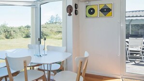 A modern dining area with a glass wall, white table, and chairs, overlooking a natural landscape. - 4 Person Holiday Home in Lokken (Lokken)