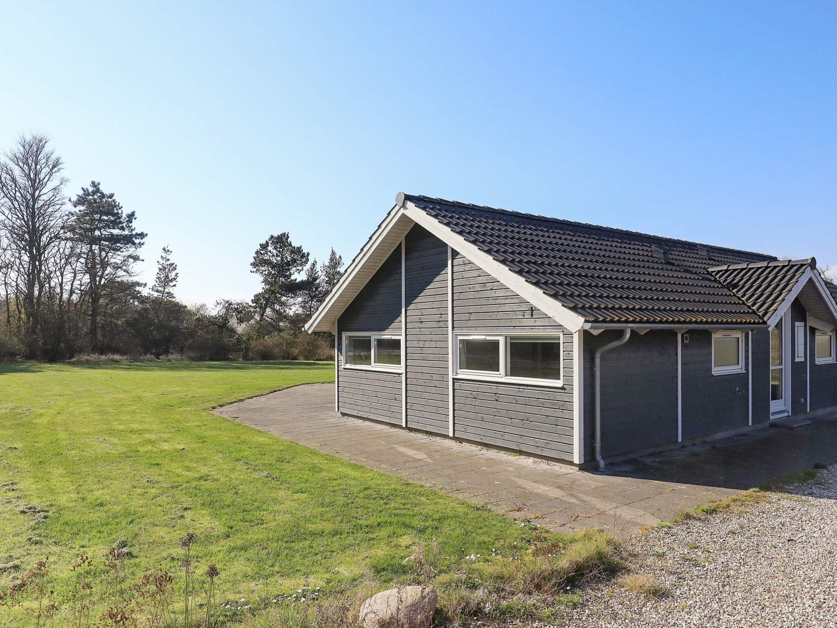 A single-story building with a gabled roof, a paved driveway, and a grassy area in the foreground.