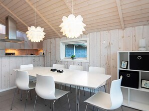 A modern kitchen with a dining table, white chairs, pendant lights, and a window with a view.