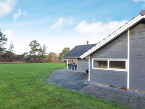 A residential property with a paved driveway, a covered outdoor seating area, and a grassy lawn.