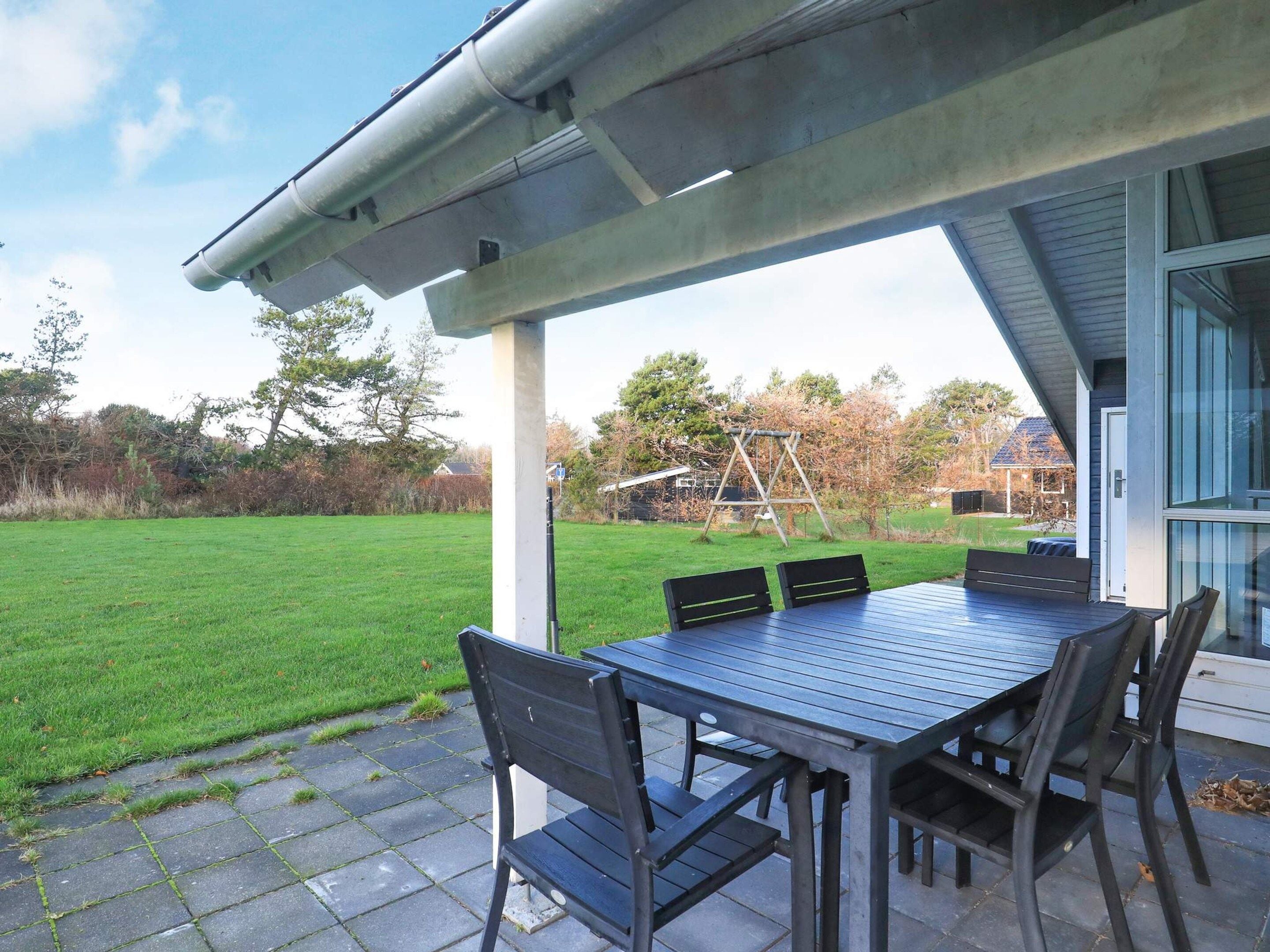 Een terras buiten met een tafel en stoelen, een schommelset en een gazon.