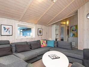A modern living room with a grey sectional sofa, a round coffee table, and wooden walls. - 8 Person Holiday Home in Humble (Sydlangeland)