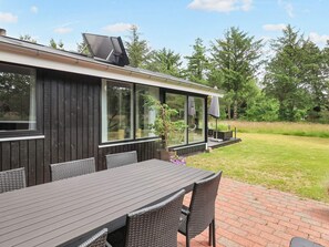 A modern outdoor dining area with a brick patio, dark wooden walls, and large windows.