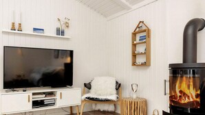 Un salon moderne avec un téléviseur, un fauteuil confortable, une petite étagère en bois et un poêle à bois.