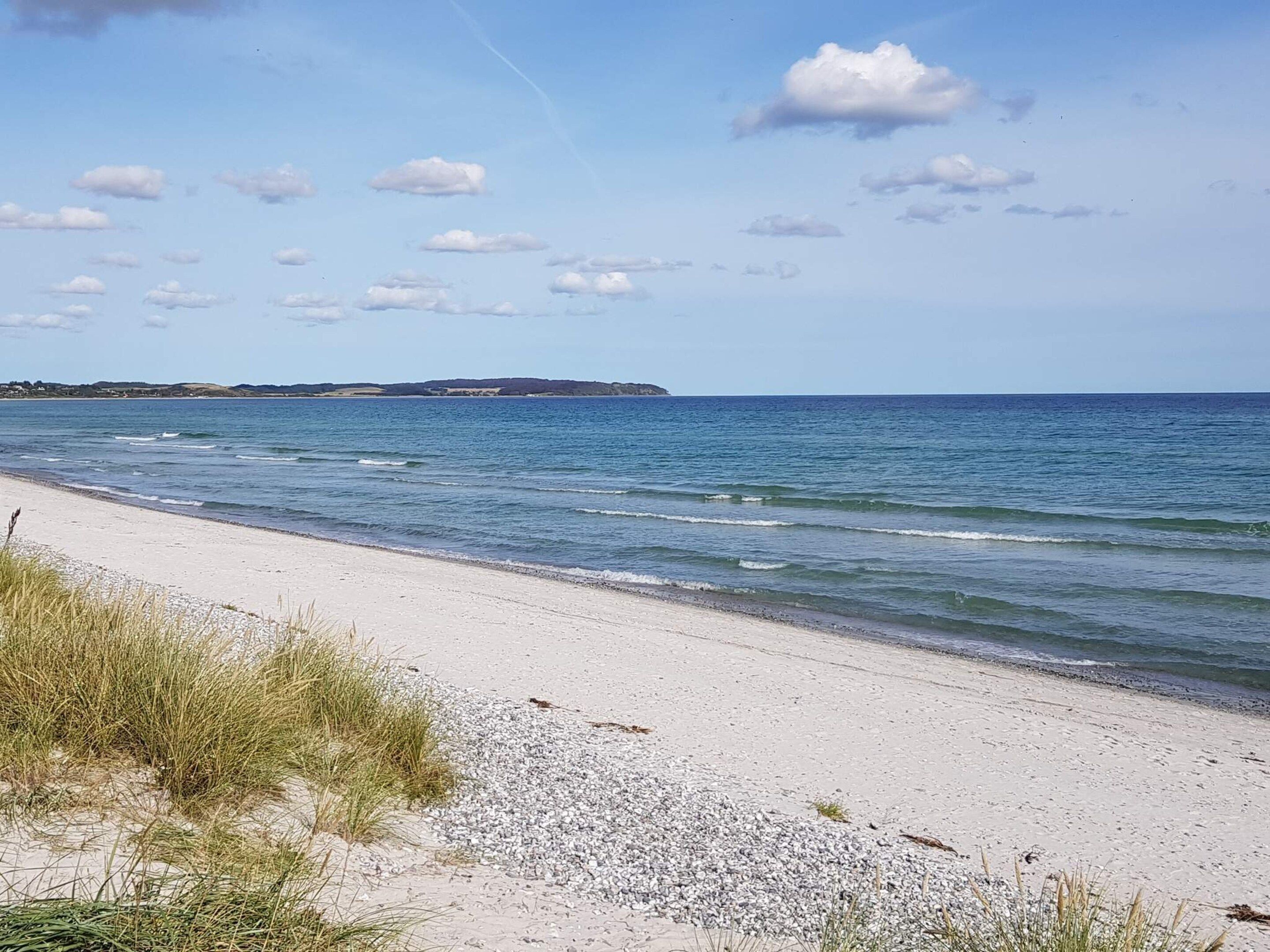 A beach with clear skies, calm waters, and distant land.