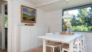 Een eetgedeelte met een witte tafel en stoelen, een schilderij aan de muur en een raam met uitzicht op groen.