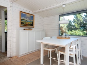 A dining area with a white table and chairs, a painting on the wall, and a window with a view of greenery. - 4 Person Holiday Home in Ebeltoft-by Traum (Ebeltoft)