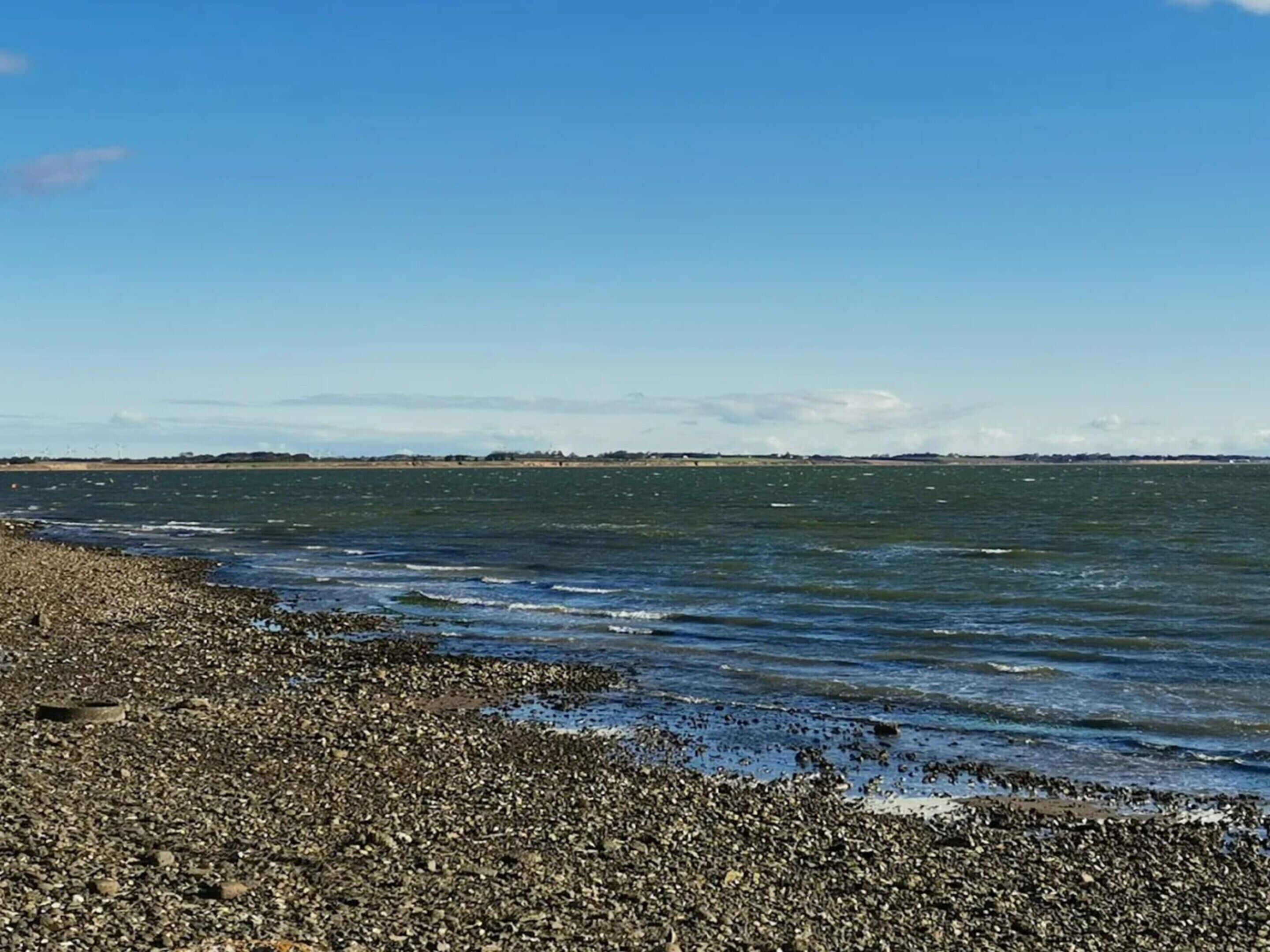 Une côte rocheuse bordée d’une mer calme et d’une terre lointaine.