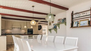 Zona pranzo con tavolo e sedie bianche, cucina sullo sfondo e soffitto con travi a vista.