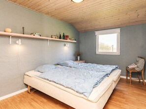 Une chambre à coucher avec un lit, une fenêtre, une chaise et une étagère contenant des livres et des bouteilles.