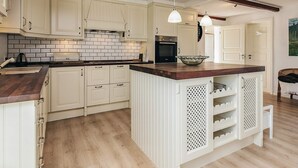 Una cucina con mobili bianchi, un piano di lavoro in legno, un'isola integrata con ripiani, illuminazione a sospensione e schienale rivestito di piastrelle.