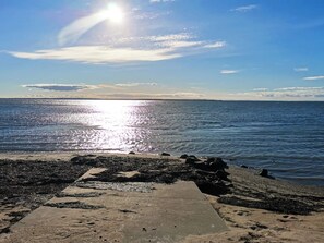 Une plage avec une promenade en béton menant à l’eau, un rivage rocheux et un ciel dégagé.