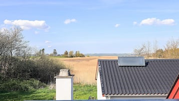 A view of a building with a tiled roof and a chimney, overlooking a field and a body of water.