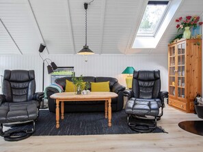 A room with a high ceiling, a skylight, a black leather sofa, two black leather chairs, a wooden coffee table, and a wooden cabinet with glass doors. - 4 Star Holiday Home in Vaeggerlose (Vaeggerlose)