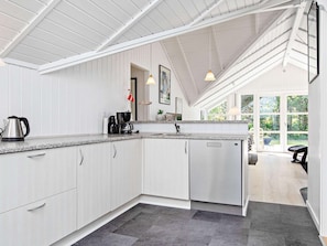 A modern kitchen with white cabinetry, a stainless steel coffee maker, and a large window providing natural light.