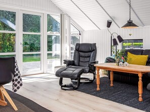 A modern living room with a leather recliner, a wooden coffee table, and a black sofa with a yellow pillow. - 4 Star Holiday Home in Vaeggerlose (Vaeggerlose)