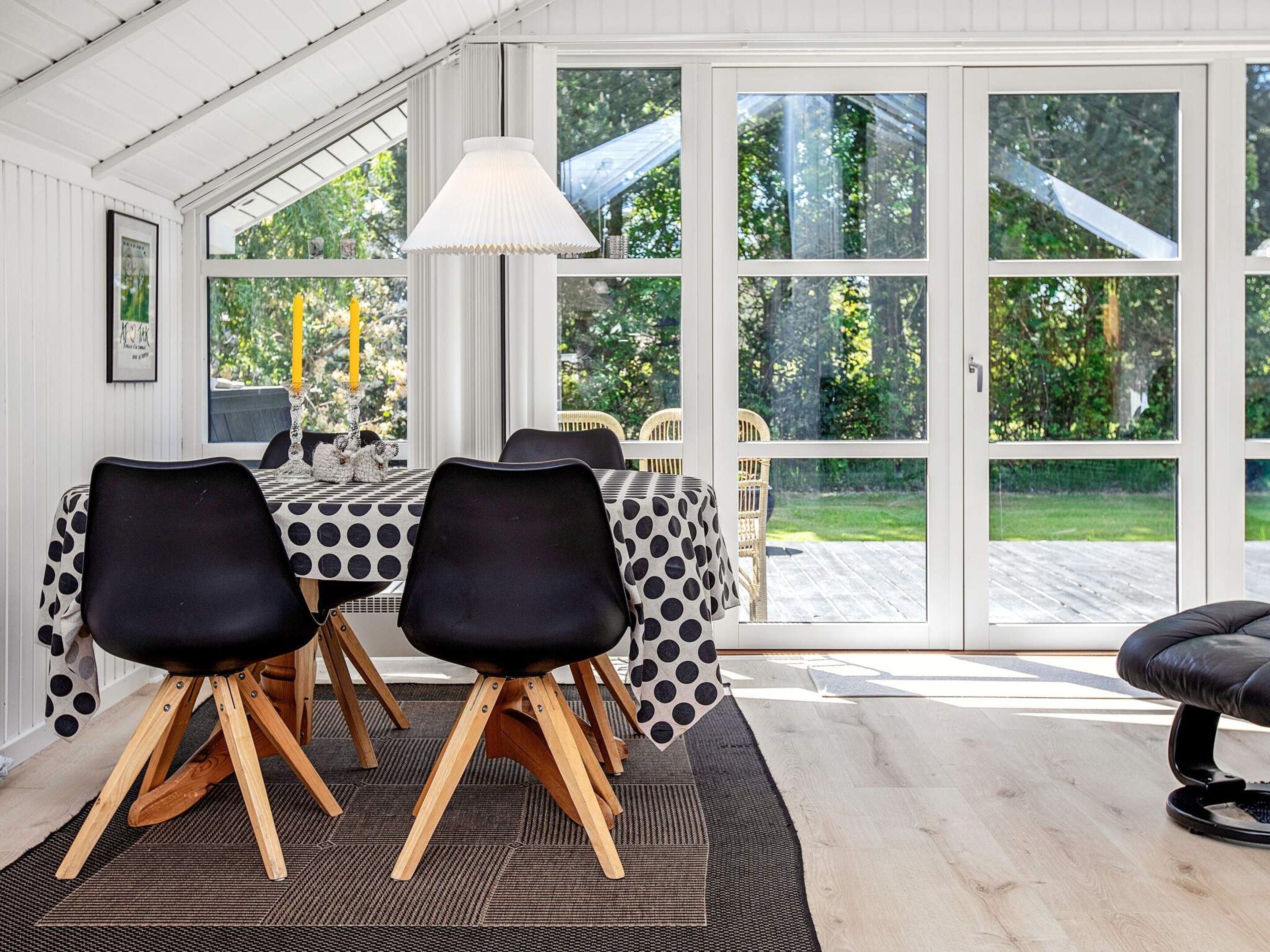 Un espace repas comprenant une table et des chaises, de grandes fenêtres et une vue sur l’extérieur.