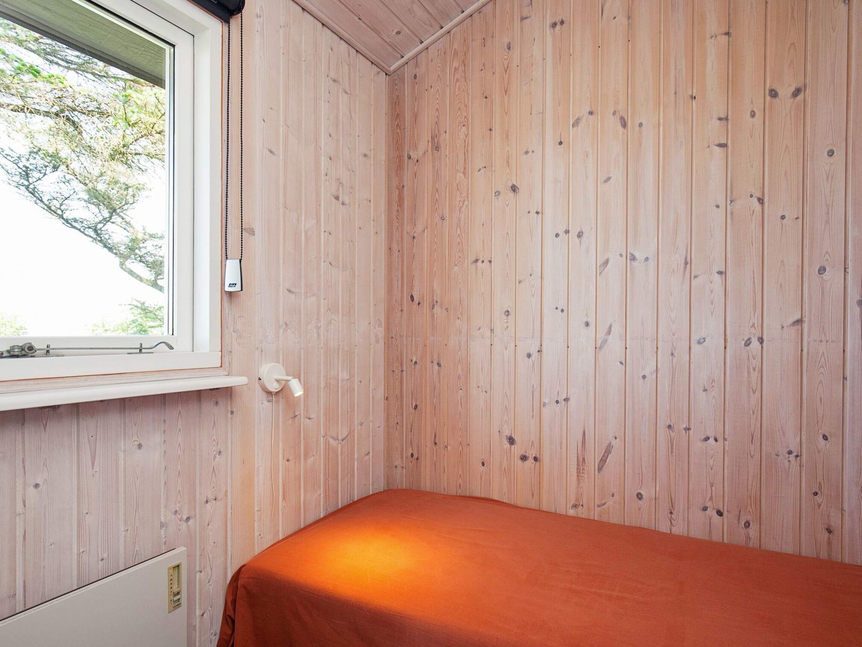 Una habitación con una cama individual, una ventana y paredes de madera.