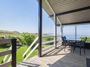 A covered outdoor area with a table and chairs, overlooking a grassy landscape and the sea. - 4 Star Holiday Home in Struer (Struer)