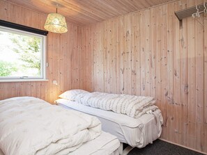 Une chambre avec un mur lambrissé en bois, un lit recouvert d’une couette à motifs et une lampe suspendue.
