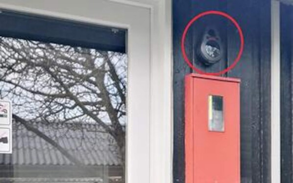 A red utility meter box mounted on a wall with a window showing bare tree branches.