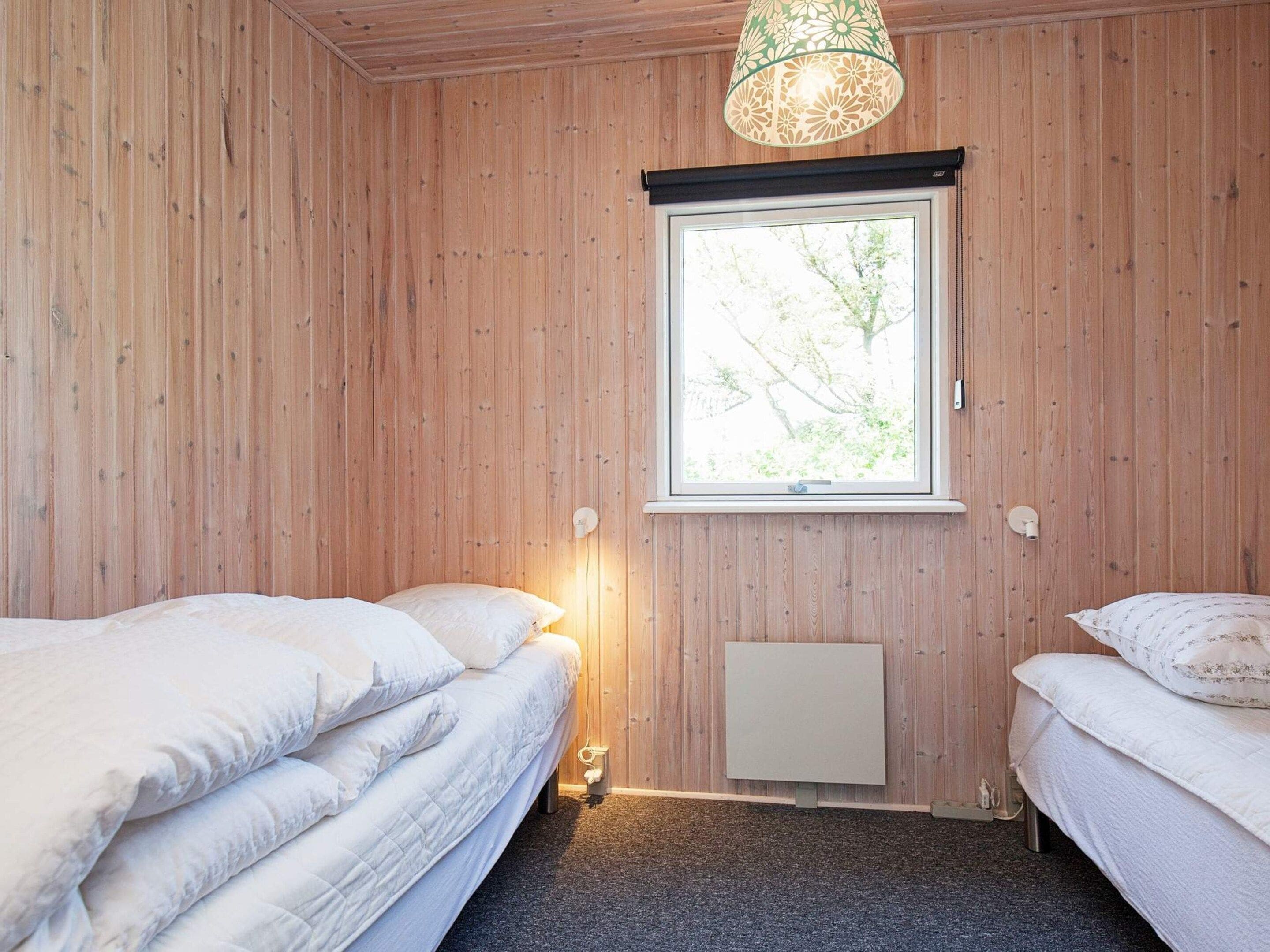 Ein Zimmer mit Holzwänden, einem Fenster mit Blick auf Bäume, zwei Betten mit weißer Bettwäsche und einer Pendelleuchte.