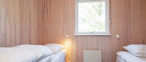 A room with wooden walls, a window with a view of trees, two beds with white bedding, and a hanging light fixture.