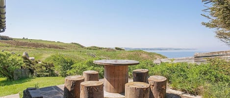 Un patio de piedra con una mesa y taburetes de madera, con vistas a un paisaje costero.