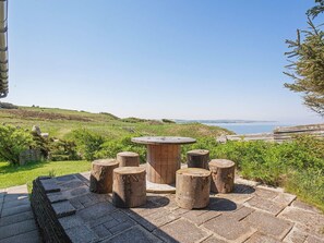 A stone patio with a wooden table and stools, overlooking a coastal landscape. - 4 Star Holiday Home in Struer (Struer)