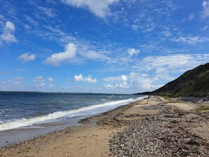 Une plage de galets, un ciel dégagé et une colline lointaine.