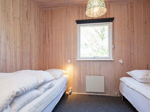 A room with wooden walls, a window with a view of trees, two beds with white bedding, and a hanging light fixture.
