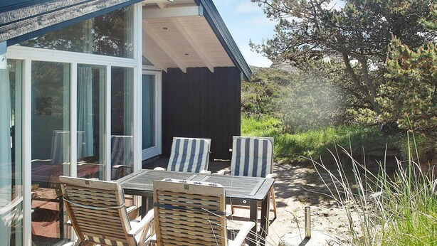 An outdoor seating area with a table and chairs, a glass door entrance, and a view of the surrounding landscape. - Spacious Holiday Home in Oksbol near Sea (Oksbol)
