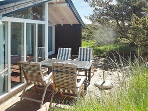 An outdoor seating area with a table and chairs, a glass door entrance, and a view of the surrounding landscape.