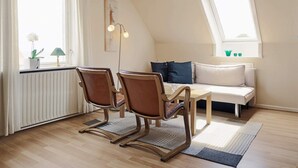 A cozy room with a wooden floor, a sofa, two chairs, a table, a floor lamp, and a window with curtains. - 4 Person Holiday Home in Allinge (Allinge)
