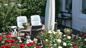 A patio with two chairs, a table, and a white umbrella. There are red and white flowers in the foreground. - 4 Person Holiday Home in Allinge (Allinge)