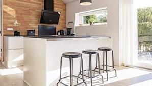 A modern kitchen with a brick wall, a large island with stools, and a window overlooking greenery. - 6 Person Holiday Home in Otterup-by Traum (Otterup)