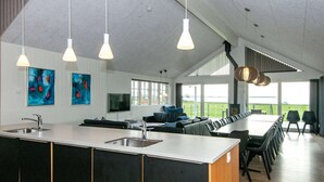 A modern kitchen with a central island, a dining area with a long table, and a living space with a sofa and TV. - 5 Star Holiday Home in Ebeltoft (Ebeltoft)