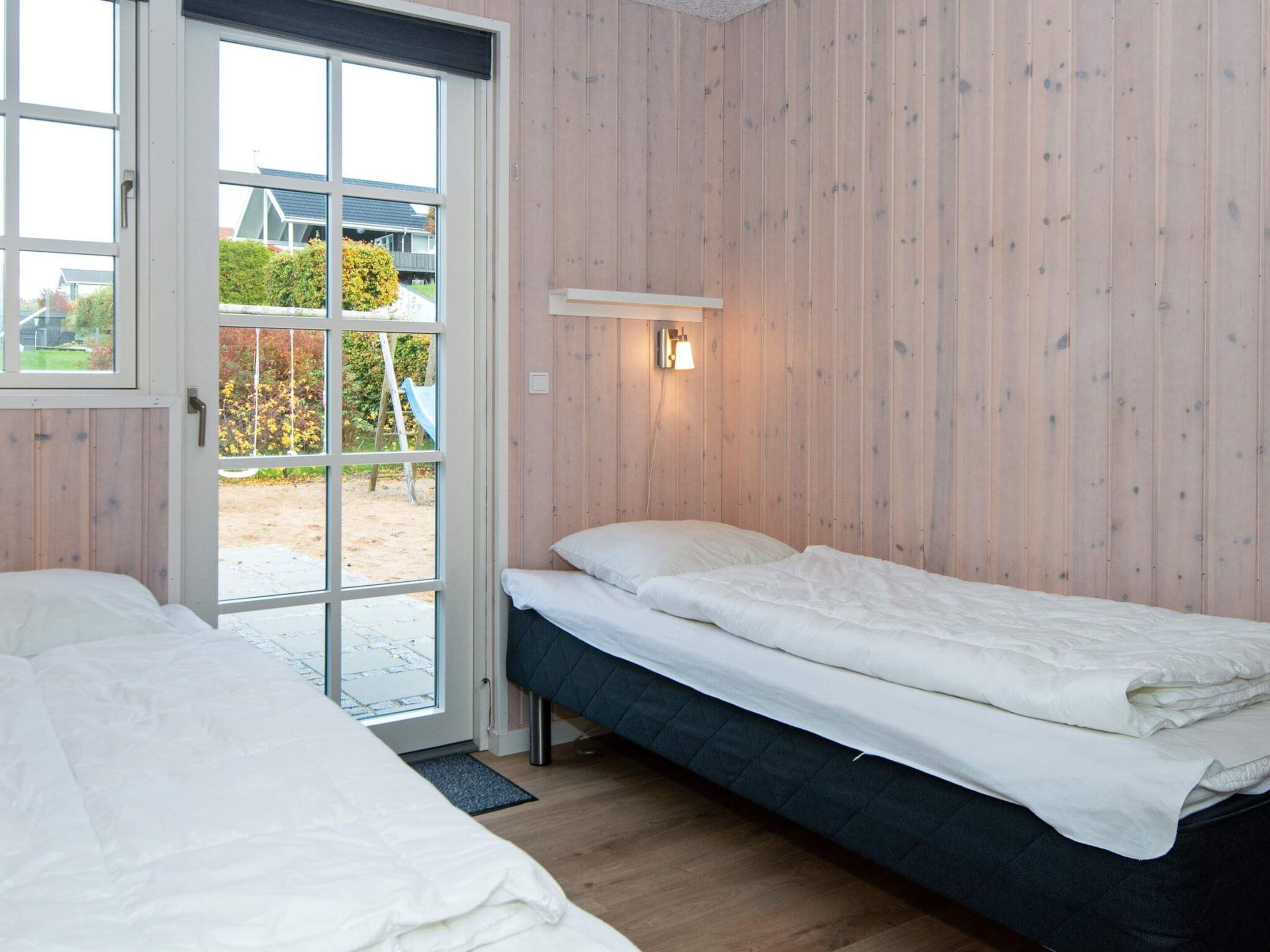 A room with two beds, a wooden wall, a door leading outside, and a wall-mounted light fixture.
