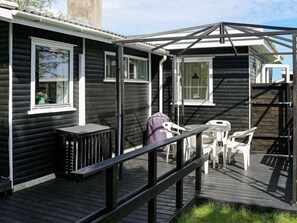 A wooden cabin with a deck, outdoor seating, and a grill.