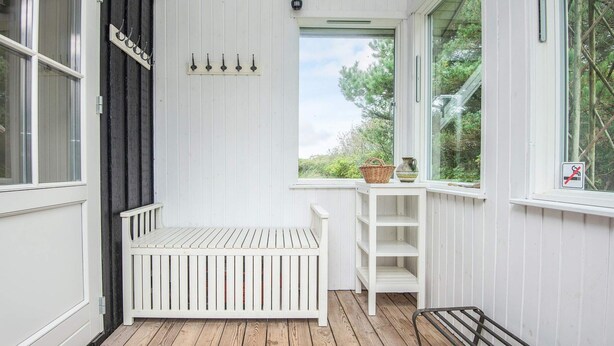 A white wooden room with a bench, a window with a view of greenery, and a door with a sign.