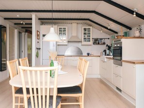 A modern kitchen with white cabinetry, a round dining table with chairs, and a hanging light fixture.