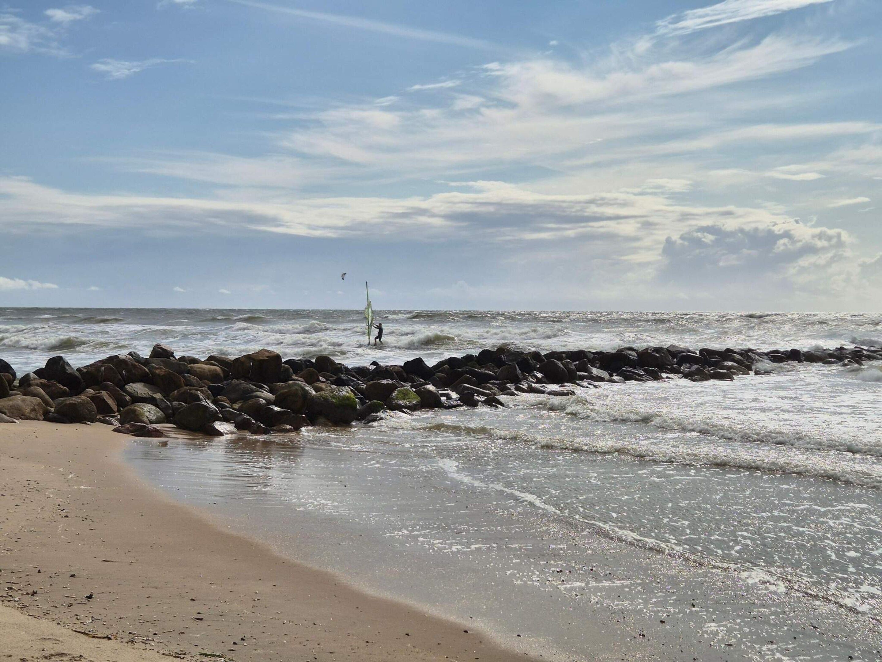 A beach with waves, a rocky breakwater, and a clear sky.