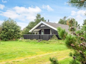 A cabin with a dark exterior, a covered porch, and a grassy yard.