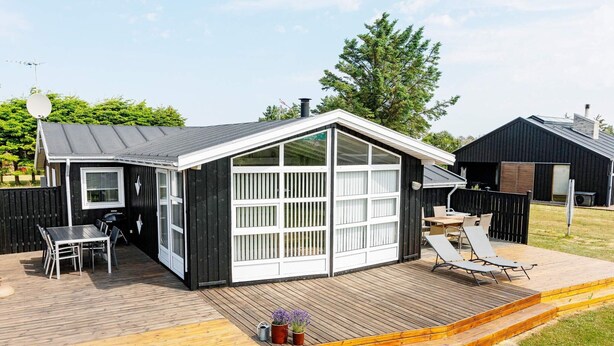 A small, black and white house with a deck, a grill, and a patio area with chairs.