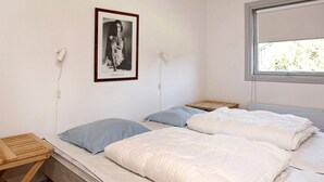 A bedroom with two beds, a wooden side table, a framed picture on the wall, and a window with a view of trees.